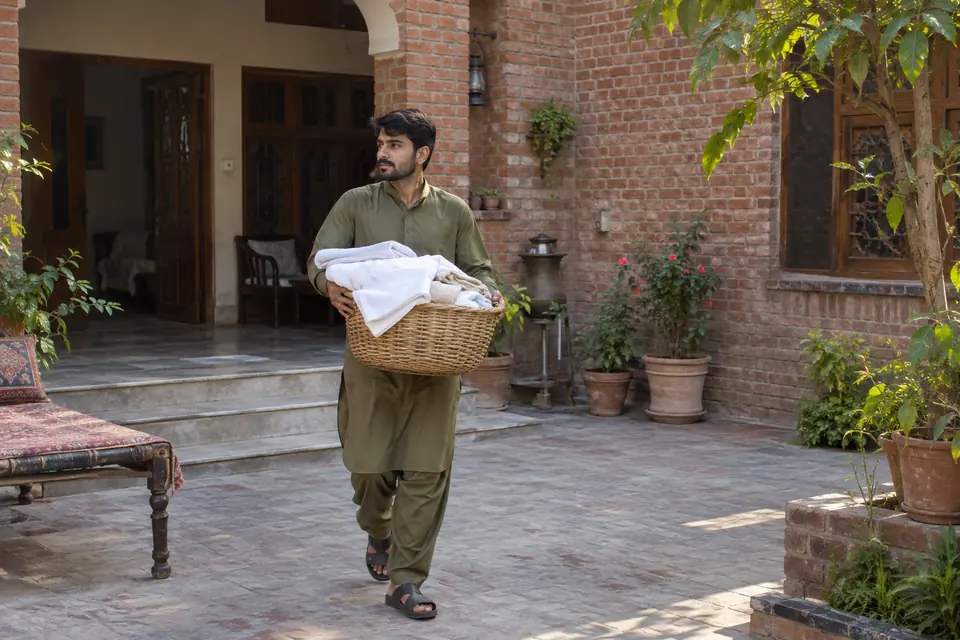 Male House Helper in Rawalpindi: Helper carrying clean linen through a courtyard